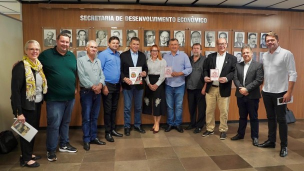 grupo de pessoas em pé, em frente a uma parede com fotos. Acima se lê "secretaria de desenvolvimento econômico"
