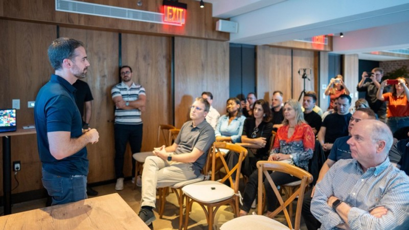 Foto do governador Eduardo Leite, usando calça jeans e camisa polo azul, falando para um grupo de pessoas que está sentado em cadeiras de madeira.