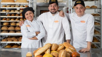 Foto de três pessoas, dois homens e uma mulher, em uma fábrica de pães. 