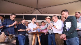 Grupo de homens, alguns aplaudem enquanto dois deles se cumprimentam dando um aperto de m&atilde;o