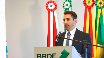 foto de uma homem branco, de terno e gravata azuis, e camisa branca
ele est&aacute; falando ao microfone atr&aacute;s de um p&uacute;lpito de madeira