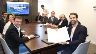 Fotografia de uma reuni&atilde;o institucional em sala de reuni&otilde;es. Oito participantes est&atilde;o sentados ao redor de uma mesa retangular de madeira, enquanto uma nona pessoa aparece em p&eacute; ao fundo. Em primeiro plano, &agrave; direita, uma pessoa sentada segura um documento aberto voltado para a c&acirc;mera. &Agrave; esquerda, outra pessoa est&aacute; posicionada na cabeceira lateral da mesa. Sobre a mesa h&aacute; notebooks fechados, cadernos, celulares e equipamentos de videoconfer&ecirc;ncia.

Ao fundo, um monitor exibe a apresenta&ccedil;&atilde;o com o t&iacute;tulo &ldquo;Programa Avan&ccedil;ar Deep Tech&rdquo;. O ambiente possui paredes claras, painel ripado escuro atr&aacute;s da tela e ilumina&ccedil;&atilde;o interna. A fotografia registra um momento de formaliza&ccedil;&atilde;o e apresenta&ccedil;&atilde;o da iniciativa, com os participantes reunidos em torno da mesa de trabalho.